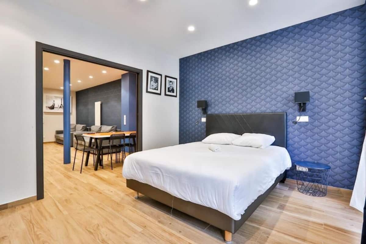 A modern hotel room with a large bed, a dining area, and a blue textured wall.