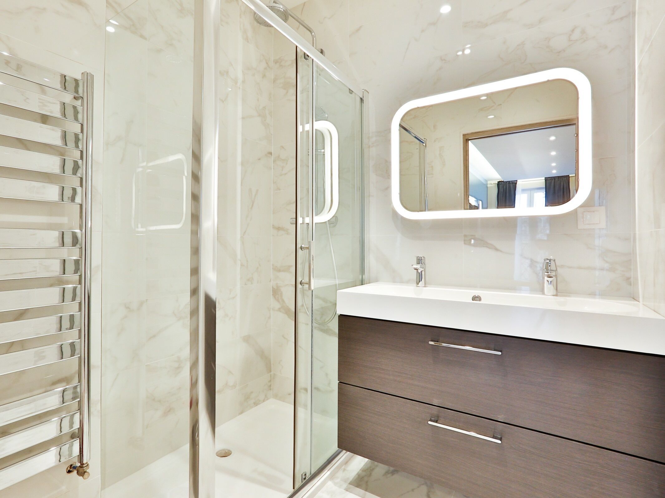 Un baño moderno con ducha de vidrio, tocador con espejo y suelo de mármol.
