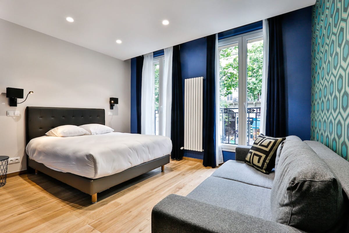 A modern bedroom with a bed, a sofa, and a window with curtains.