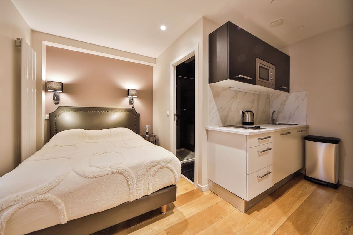 A bedroom with a bed, bedside lamps, a nightstand, and a view into a bathroom.