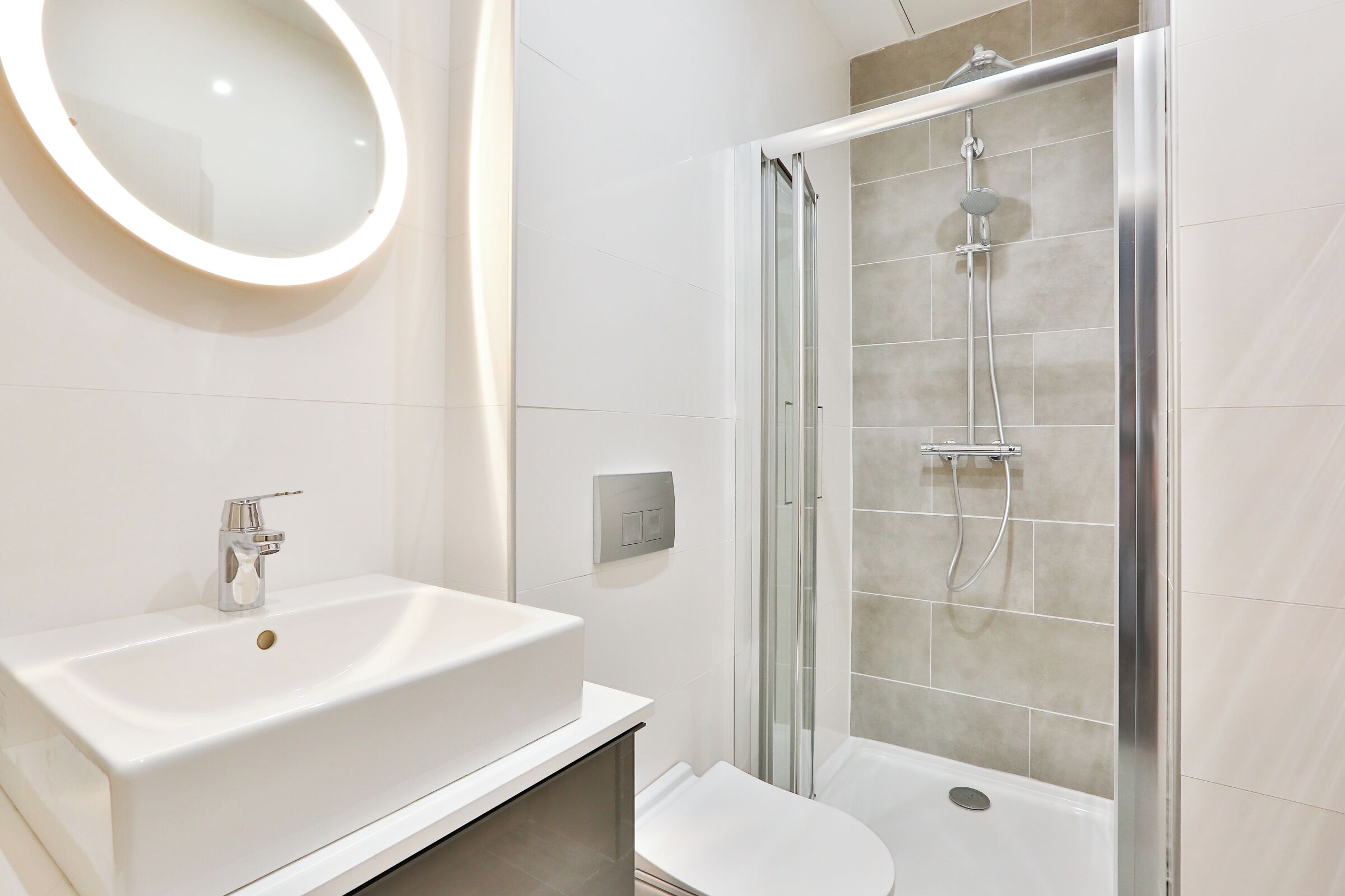 Een moderne badkamer met een witte wastafel, een spiegel en een douche met glazen wanden.