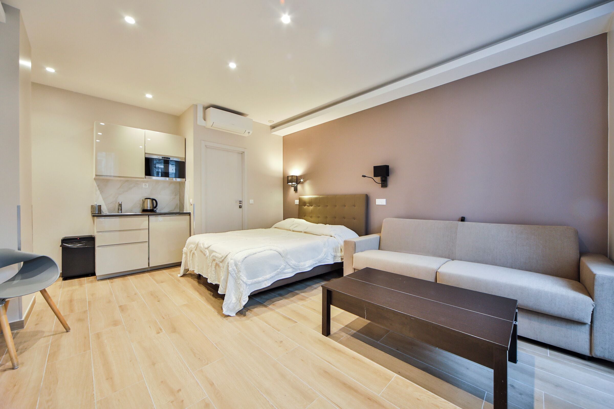 Een moderne hotelkamer met een bed, een slaapbank, een salontafel, een kitchenette en een badkamer.