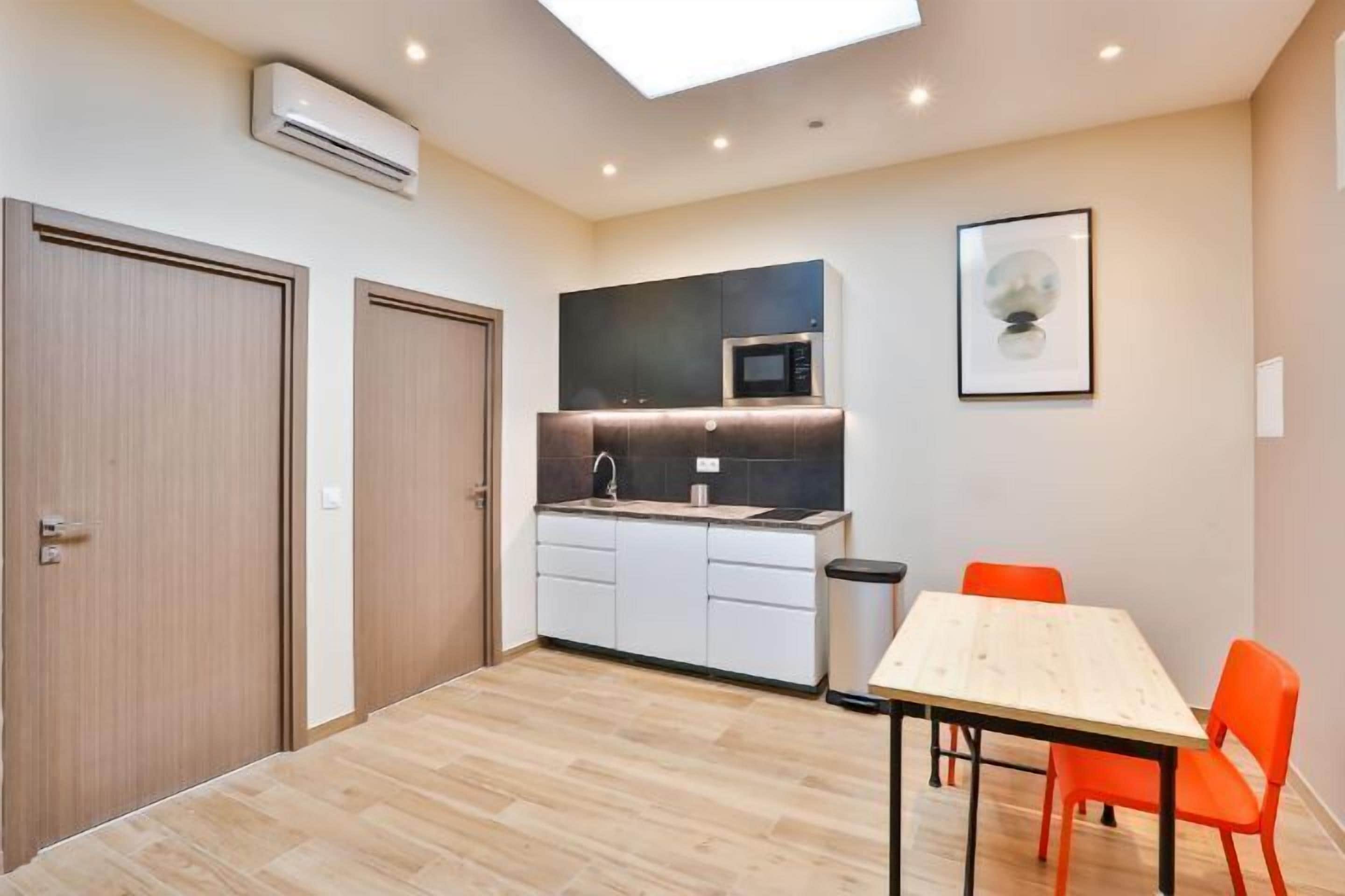 Una cocina compacta con microondas, lavamanos y armarios, una mesa de comedor con sillas y un tragaluz.