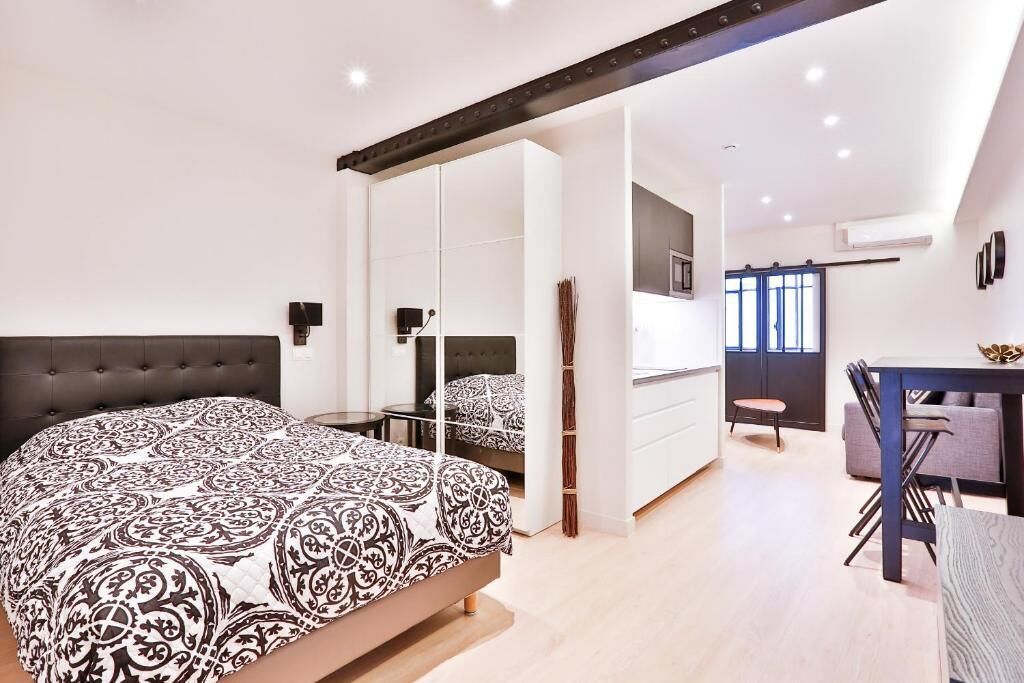 A modern bedroom with a large bed, a desk, and a chair, and a view of the city through large windows.