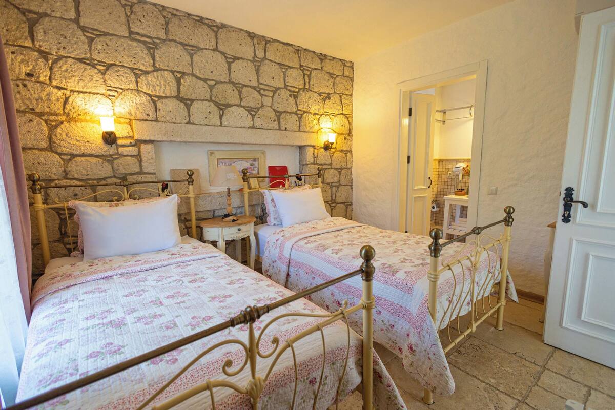 A bedroom with two beds, stone walls, and a stone fireplace.