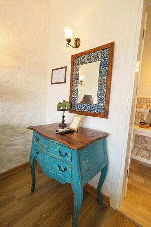 A blue wooden dresser with drawers, a framed mirror with a decorative frame, a wall-mounted light fixture, and a small shelf with decorative items. - Kupina Otel (Cesme)
