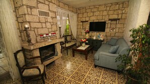 A stone-walled living room with a fireplace, a sofa, and a television mounted on the wall.