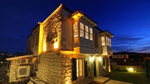 A stone house with a balcony, a small garden, and a well-lit entrance. - Kupina Otel (Cesme)