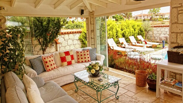 A cozy patio area with a cushioned sofa, a glass coffee table, and a view of a pool and garden. - Kupina Otel (Cesme)