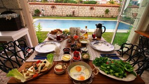 A dining table set with breakfast items, a view of a swimming pool, and outdoor furniture. - Kupina Otel (Cesme)