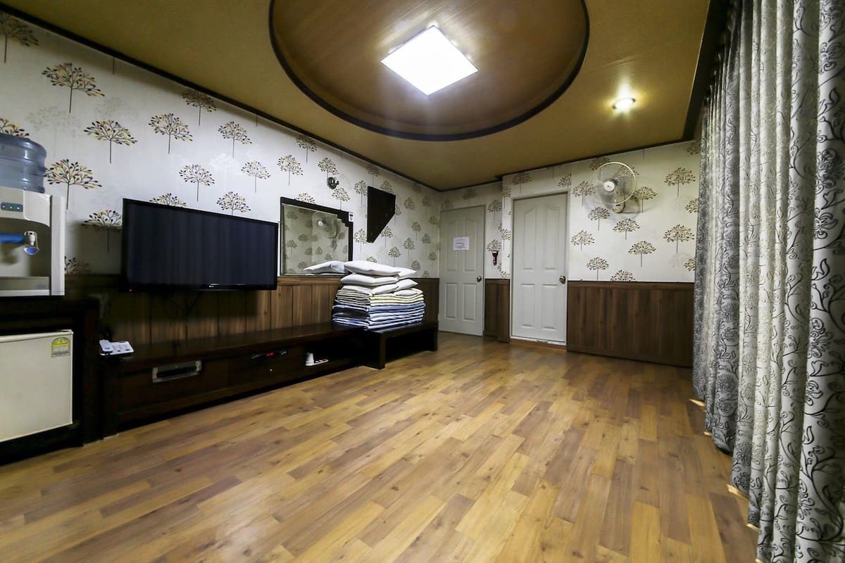 A hotel room with a wooden floor, a flat-screen TV, a water dispenser, a bed with neatly folded linens, and a ceiling fan.