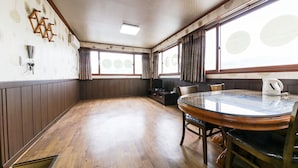 A room with a wooden floor, a round glass table with chairs, a television, and a kettle on the table. - Venus Motel&Pension (Boryeong)