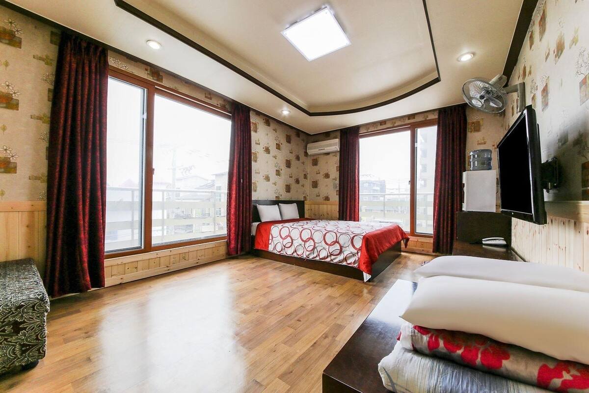 A hotel room with a large bed, a TV mounted on the wall, and a view of the city through large windows.