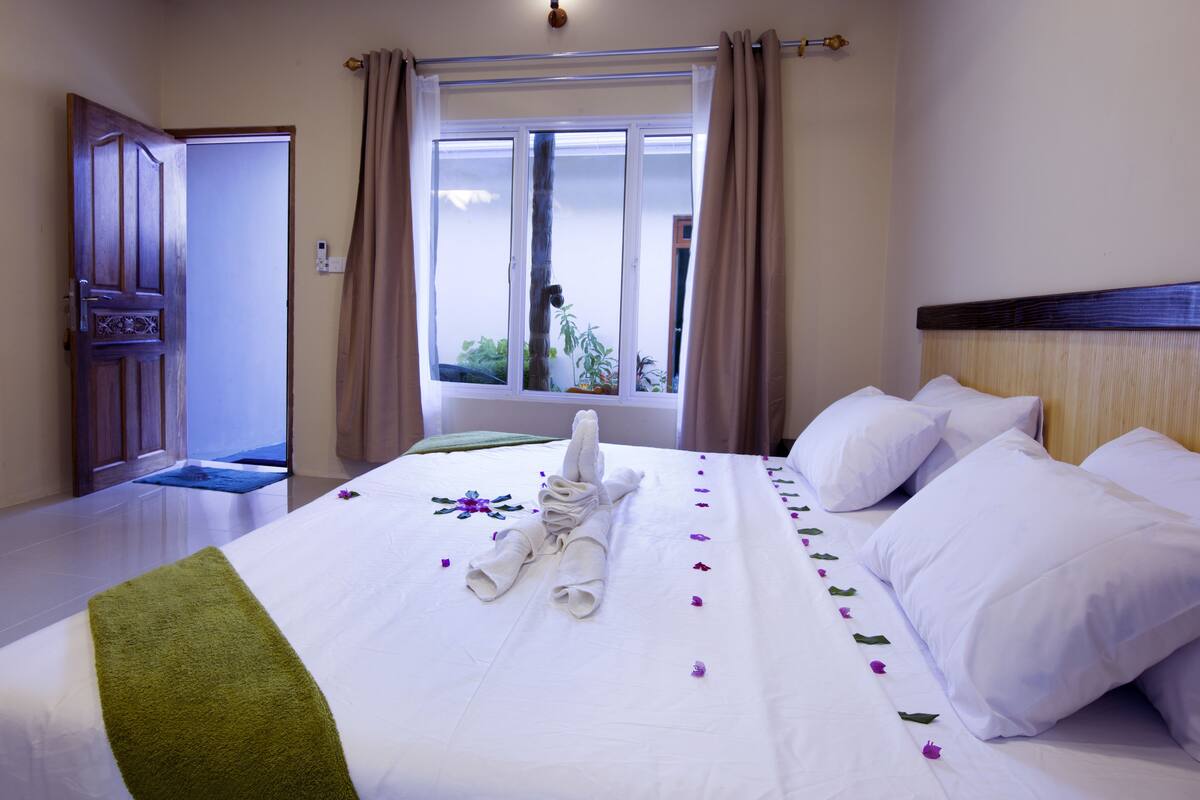 Una cama bien hecha con una toalla verde y ropa de cama blanca, una ventana con cortinas y una puerta de madera.