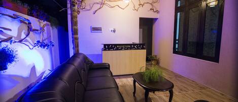 A modern reception area with a reception desk, a black leather sofa, and a small table with a plant.