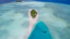 Vue aérienne d’une île tropicale aux eaux turquoise et limpides, avec une étroite plage de sable qui mène à une petite île verdoyante.
