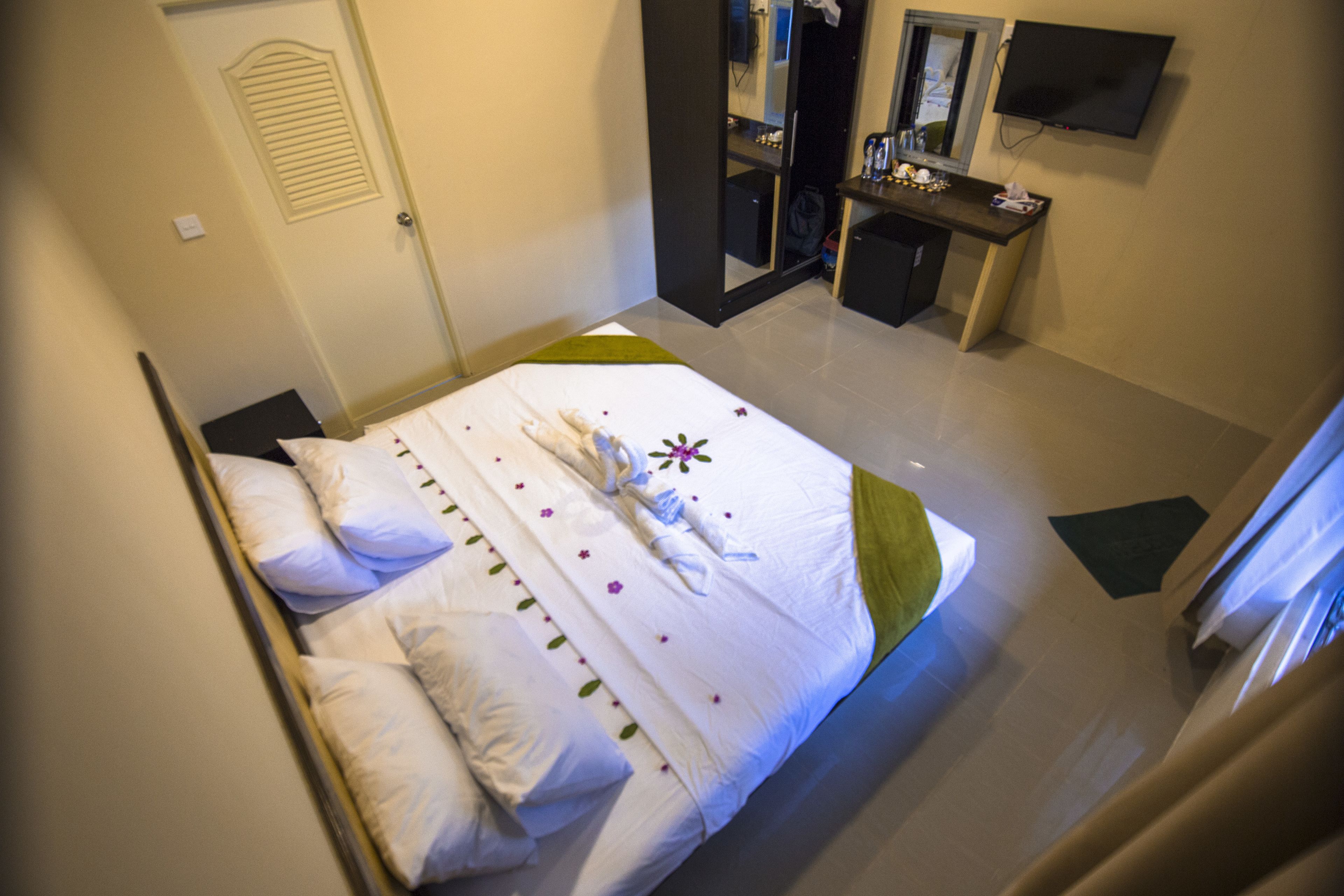 A hotel room with a neatly made bed, a desk with a mirror, and a television on the wall.