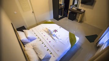 A hotel room with a neatly made bed, a desk with a mirror, and a television on the wall.