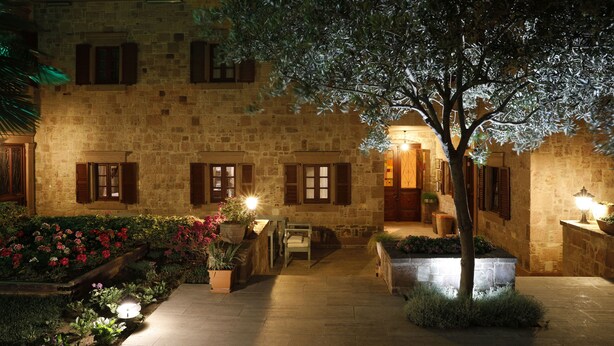 Un bâtiment en pierre avec des volets en bois, un jardin agrémenté de plantes en pot et un banc.