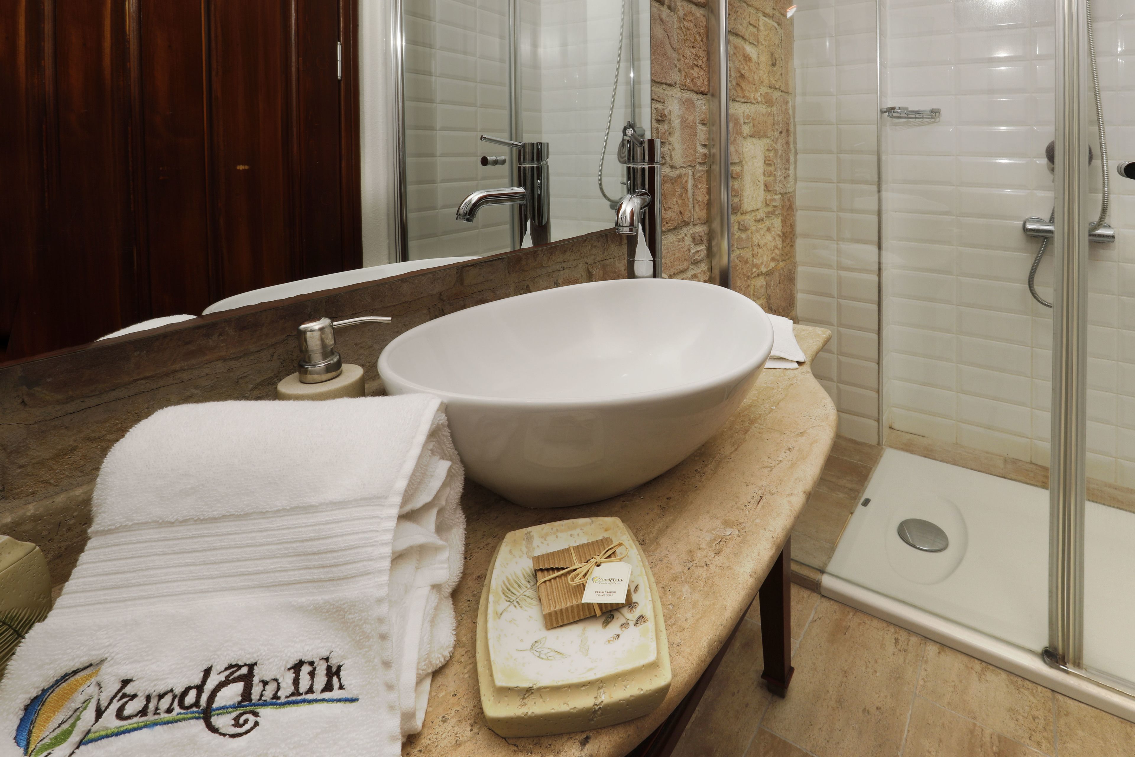 A bathroom with a large white sink, a mirror, a shower, and a towel rack.