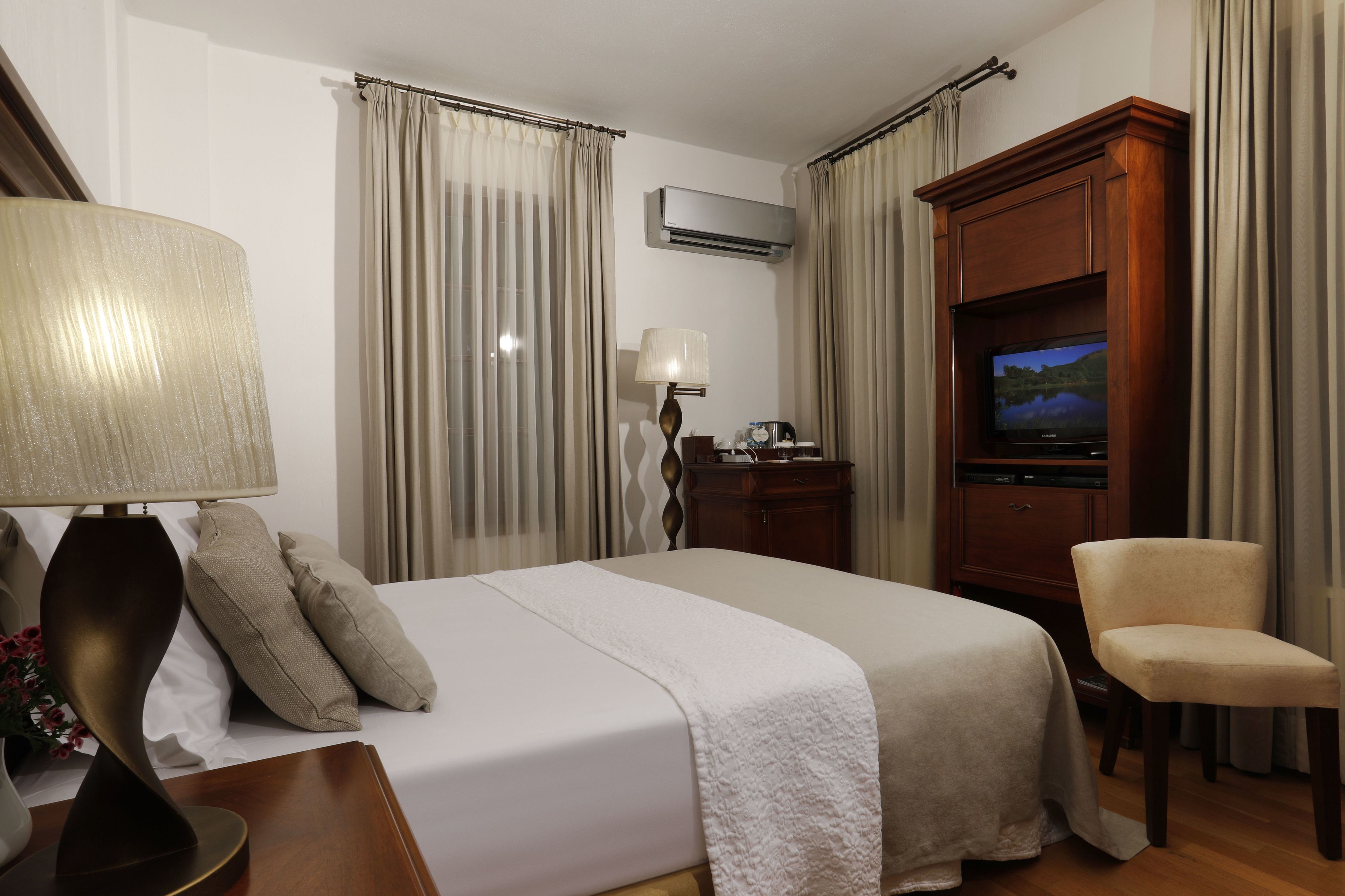 Ein Hotelzimmer mit Bett, Fernseher, Sessel und Schreibtisch mit Lampe.
