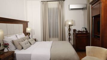 Habitación de hotel con una cama grande, lámparas de noche, una mesita de noche de madera, un escritorio con lámpara, un televisor y una silla.