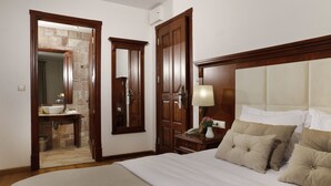 Une chambre à coucher avec un grand lit, une armoire en bois, une table de chevet avec une lampe, et une salle de bain visible à travers une porte ouverte.
