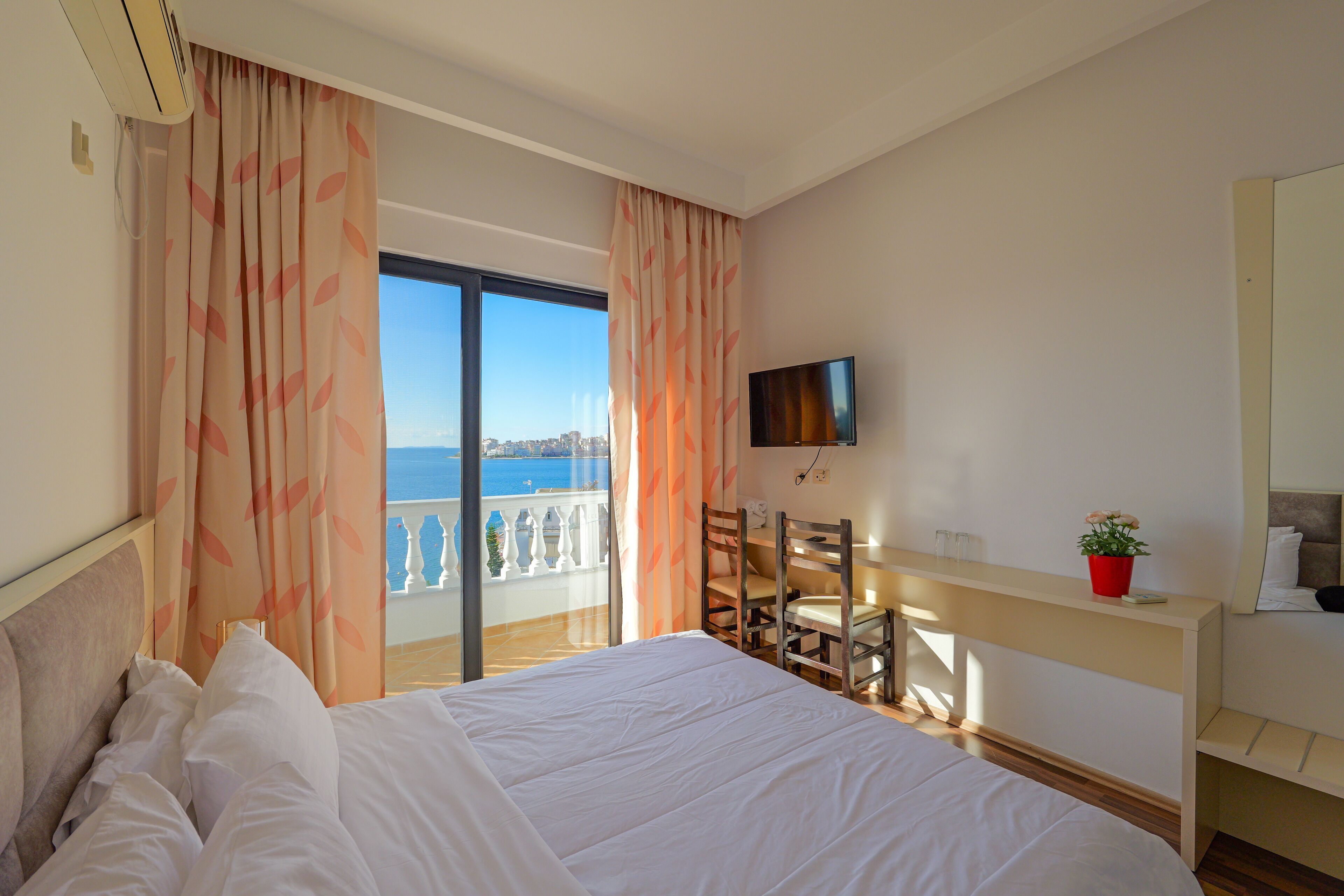 Habitación de hotel con cama, televisión, escritorio y balcón con vistas.