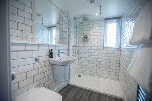 A modern bathroom with white subway tiles, a white sink, a glass-enclosed shower, and a window with blinds. - McKays Hotel Bar & Restaurant (Pitlochry)