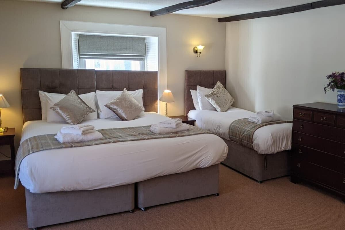 A double bed with a headboard, two bedside tables with lamps, a dresser, and a window with blinds.
