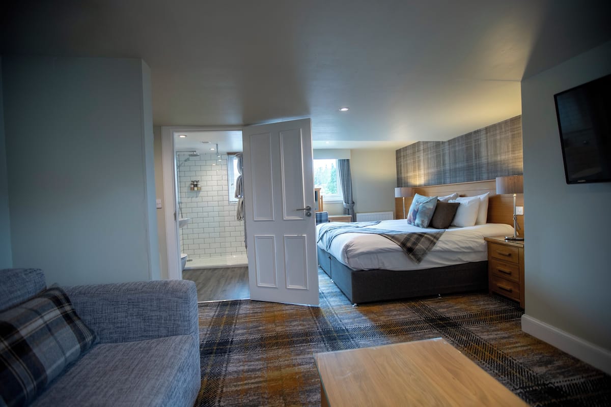 A modern bedroom with a large bed, bedside tables, a wooden bench, and a view of the bathroom.