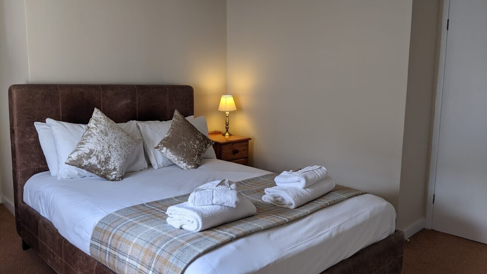 Een net opgemaakt bed met witte lakens, een geruit plaid en opgerolde handdoeken.