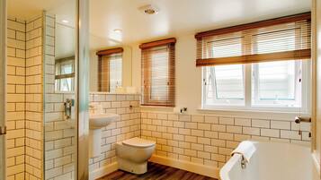 Un baño con inodoro, lavamanos y bañera, con persianas de madera y paredes de azulejos blancos.
