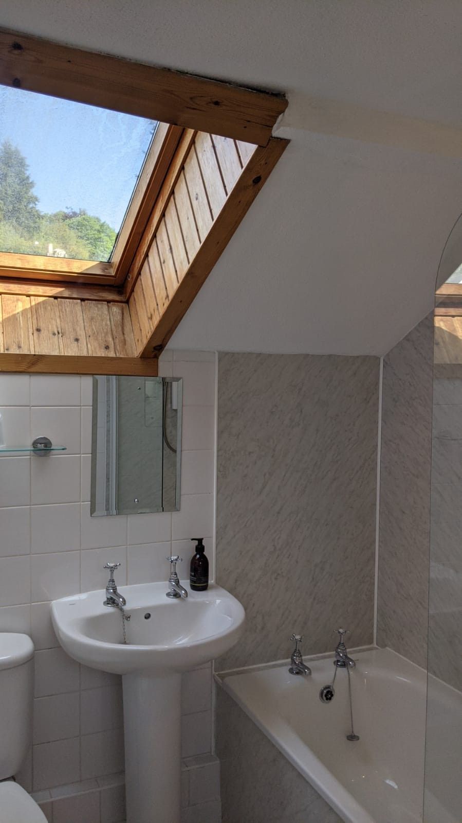 Un bany amb una finestra panoràmica, un lavabo, un mirall, un vàter i una banyera.