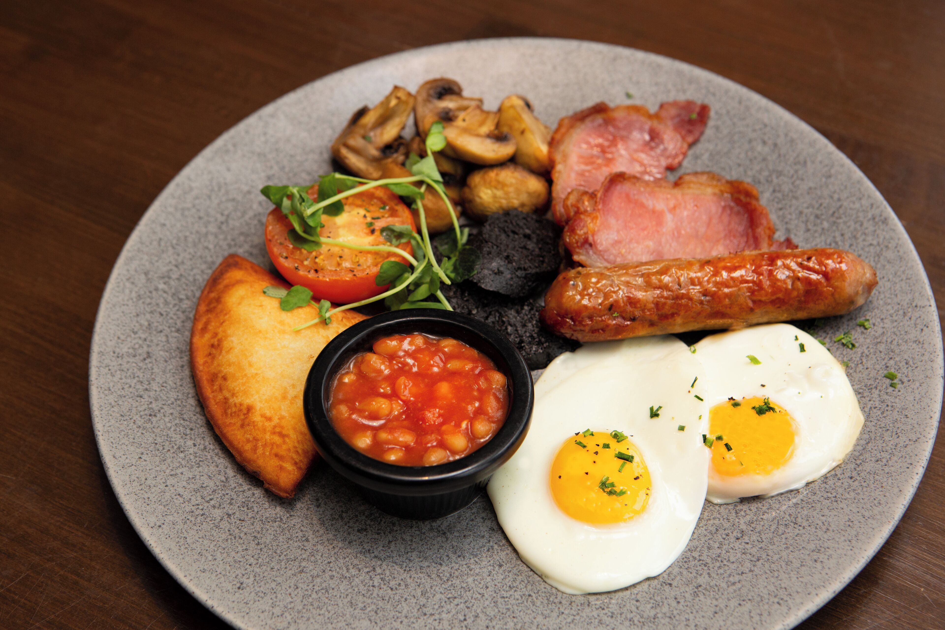 A plate of breakfast food including eggs, sausages, mushrooms, tomatoes, beans, and toast.