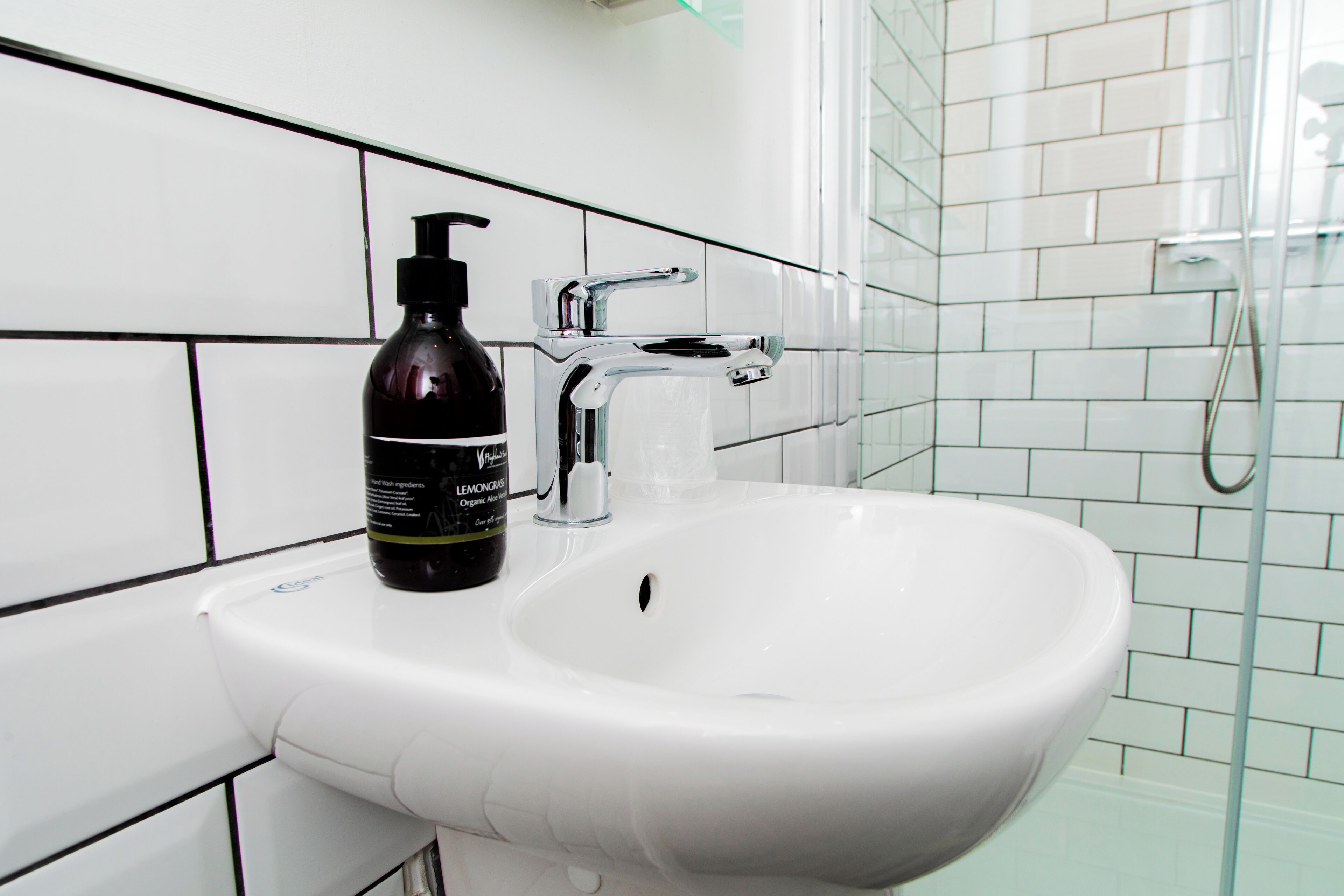 A bathroom with a white sink, a black bottle of shampoo, and a chrome faucet.