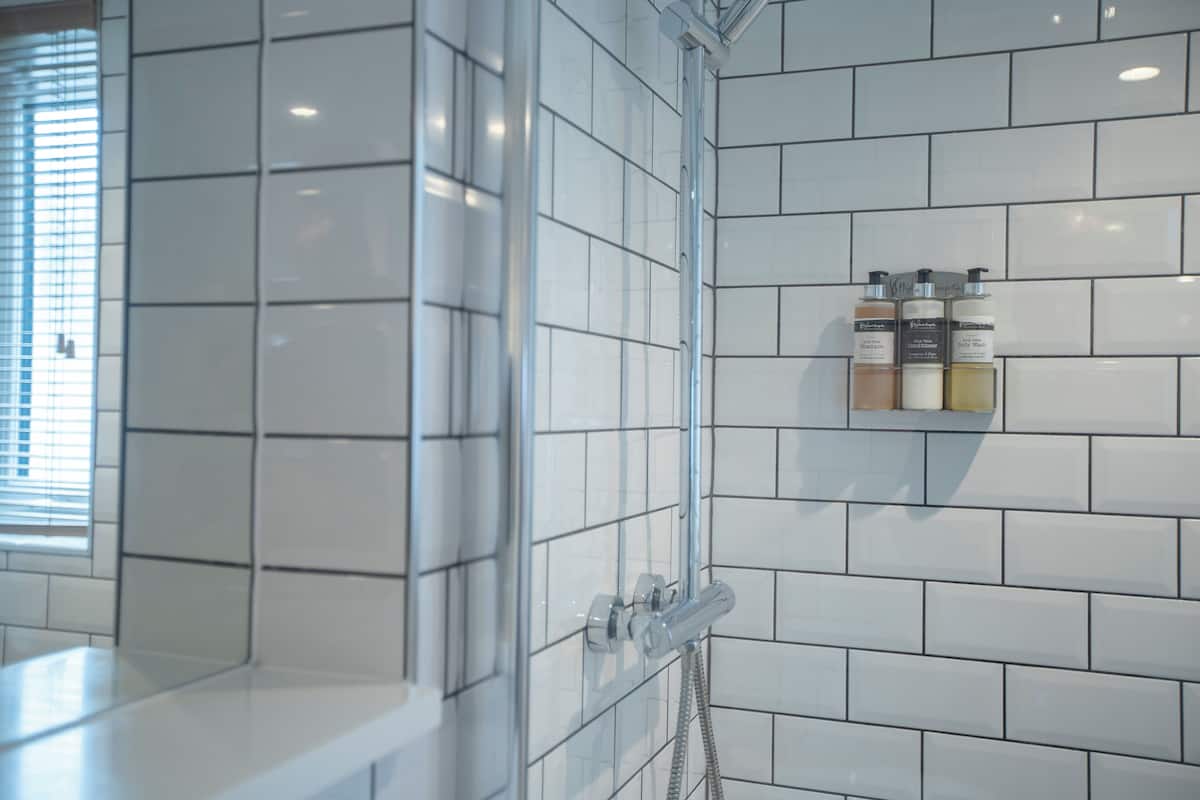 A bathroom with white tiled walls, a glass shower enclosure, and a shelf with toiletries.