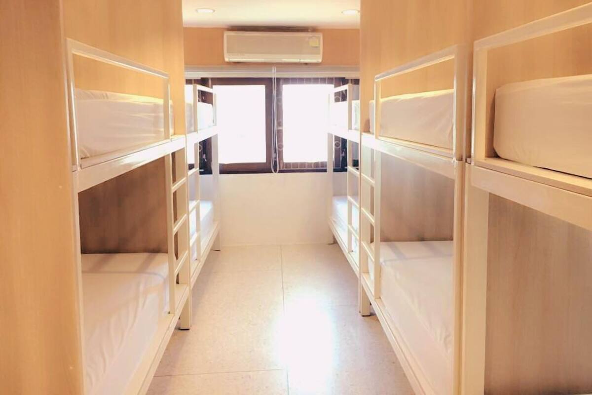 A narrow corridor with bunk beds on either side, a window at the end, and an air conditioning unit on the wall.