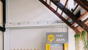 A yellow Krungsri ATM machine in a modern indoor setting with a wooden lattice wall and hanging plants. - Boon Street Hostel (Bangkok)
