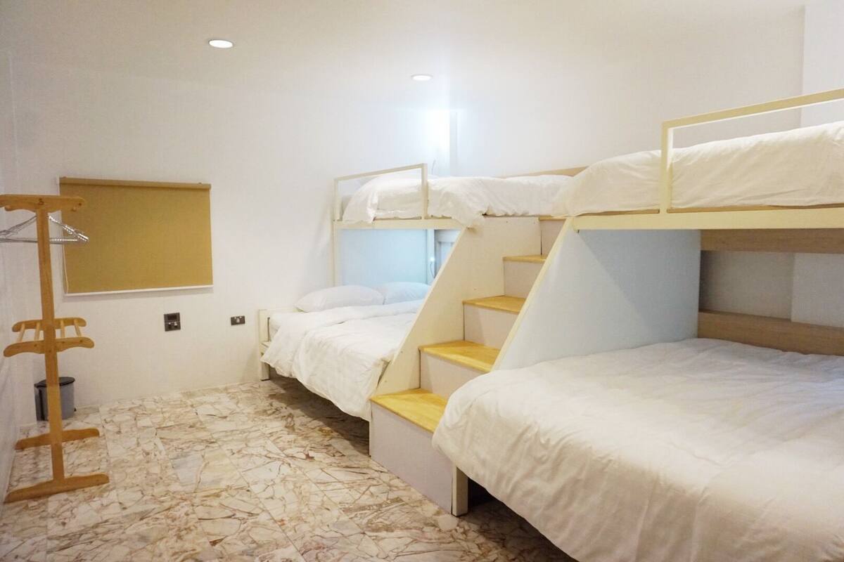 A dormitory room with bunk beds, a wooden ladder, a small window, and a marble-patterned floor.