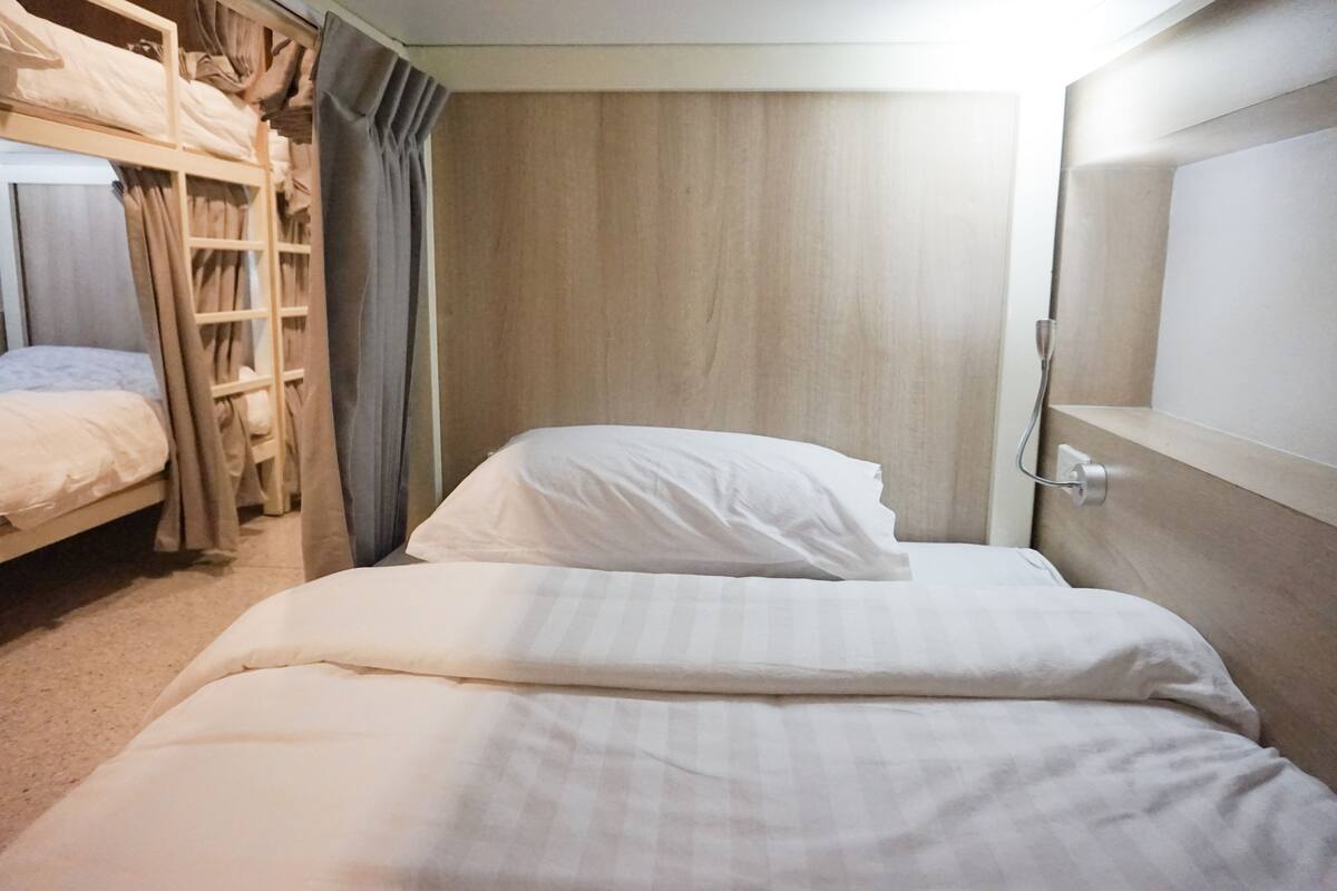 A bunk bed room with a wooden headboard, a bedside table, and a curtain.