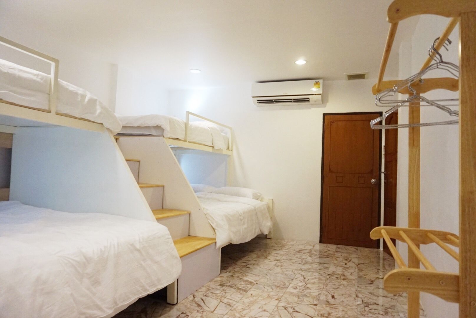 A dormitory room with bunk beds, a wooden chair, a metal hanger rack, and an air conditioning unit.