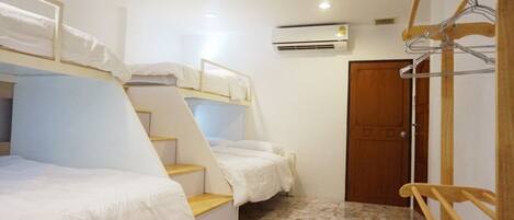 A dormitory room with bunk beds, a wooden chair, a metal hanger rack, and an air conditioning unit.