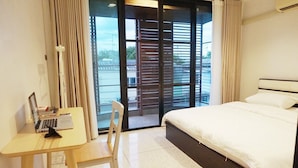 A hotel room with a bed, a desk with a laptop, a chair, and a view through a glass door. - Boon Street Hostel (Bangkok)