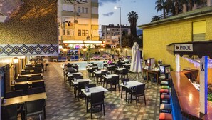 An outdoor dining area with tables and chairs, a pool, and a bar area with a sign indicating the pool direction. - Wasa Hotel (Alanya)