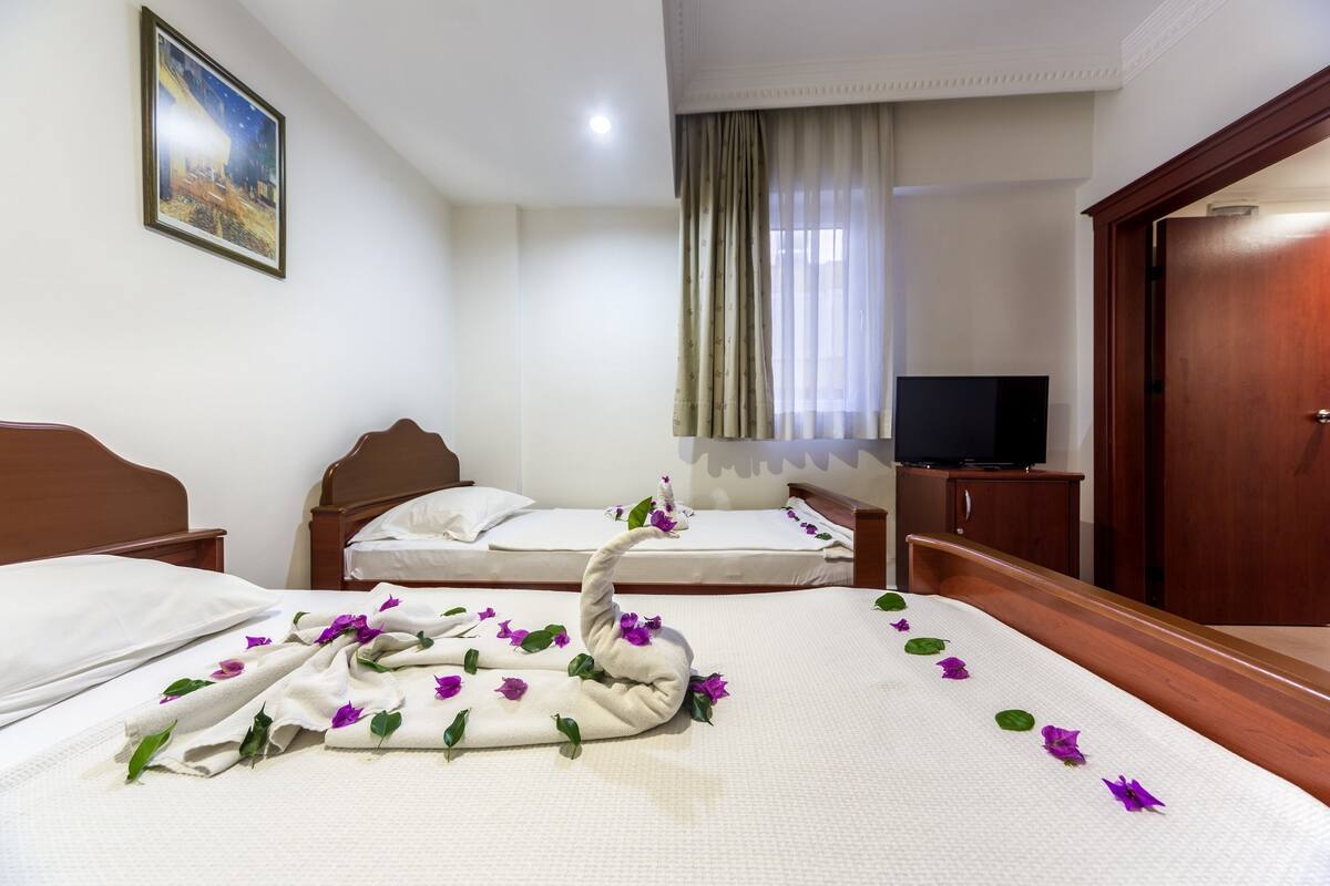 A hotel room with two beds, a television, a wooden wardrobe, and a painting on the wall.