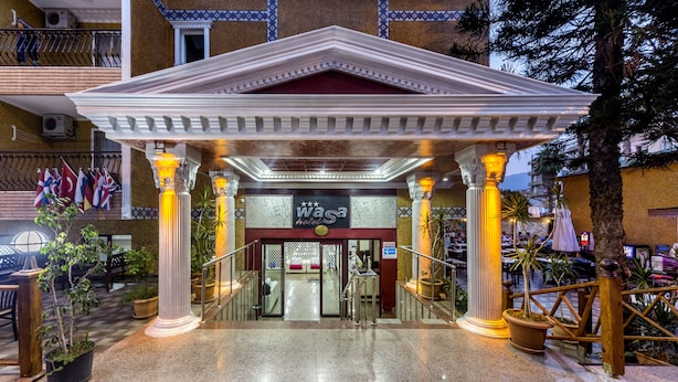 A hotel entrance with a covered walkway, columns, and a sign for a 'W' hotel. - Wasa Hotel (Alanya)