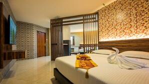 Een hotelkamer met een groot bed, een houten scheidingswand, een zichtbare badkamer door de wand heen en een aan de muur bevestigde televisie.