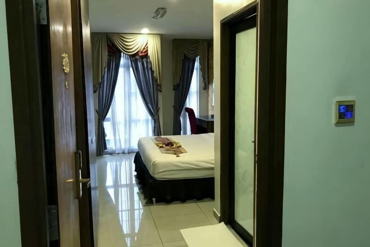 Habitación de hotel con cama, cortinas, una silla y un panel de control en la pared.