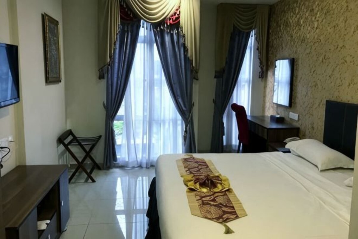 Habitación de hotel con cama, escritorio, silla, televisor y cortinas.